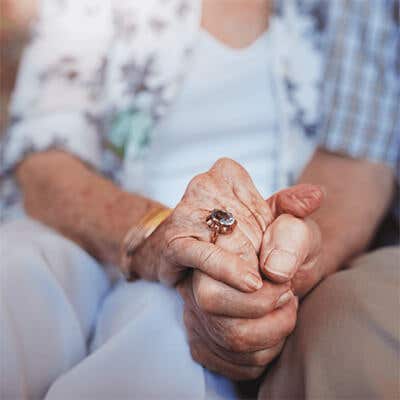 A man and woman holding hands. The woman is wearing a beautiful gemstone ring. 